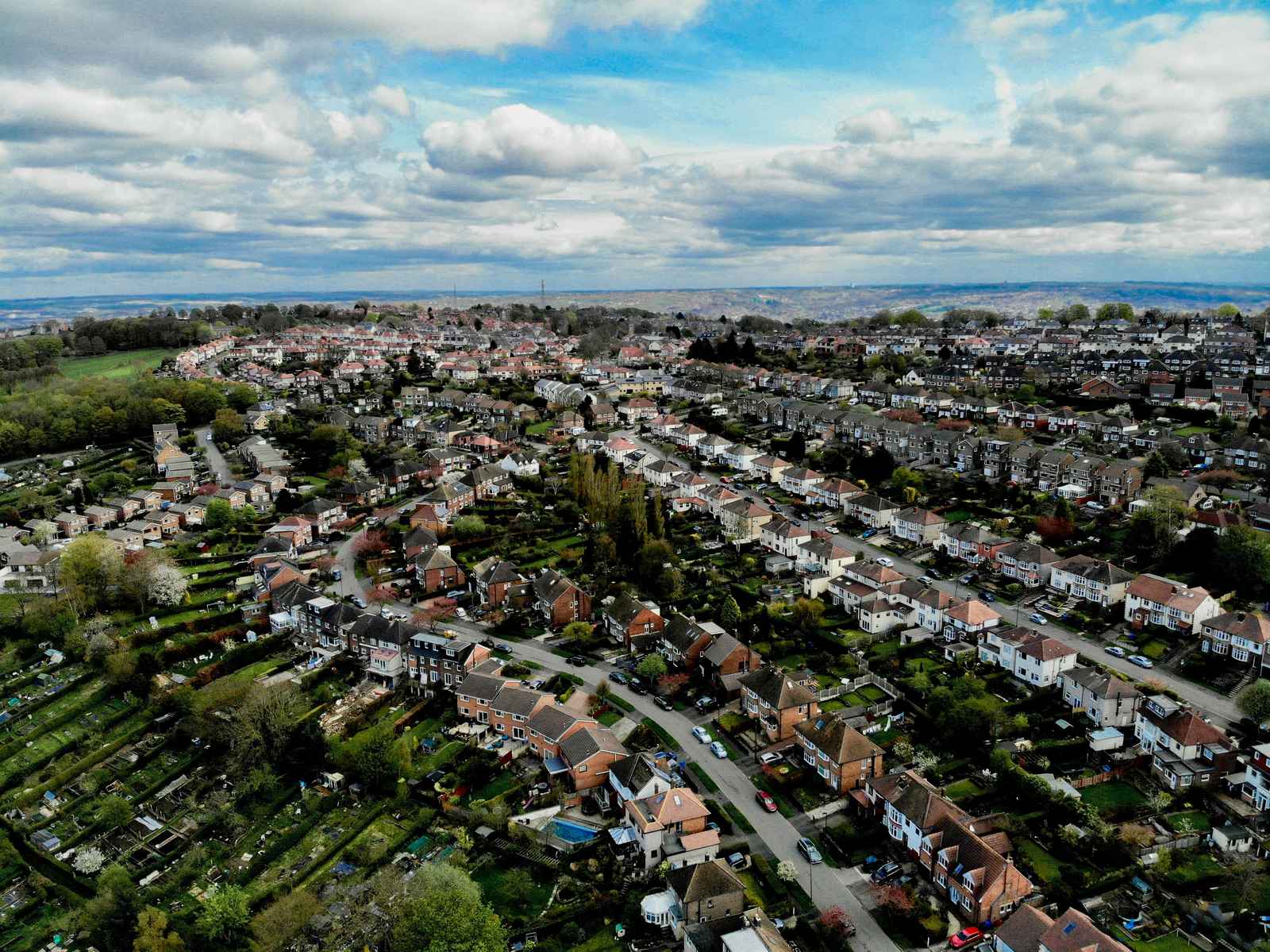 An aerial view of a residential area with many houses and green spaces under a cloudy sky