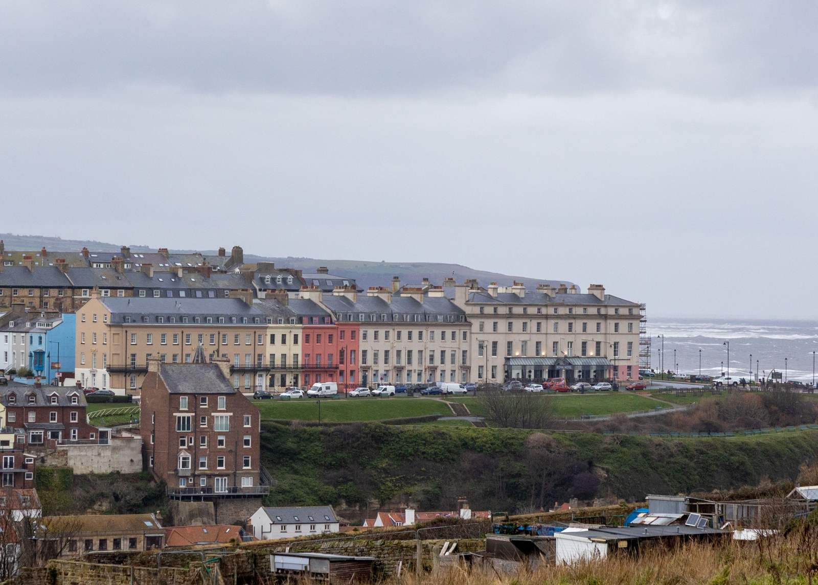 A coastal town with many buildings on a hillside overlooking a rough sea under a grey sky