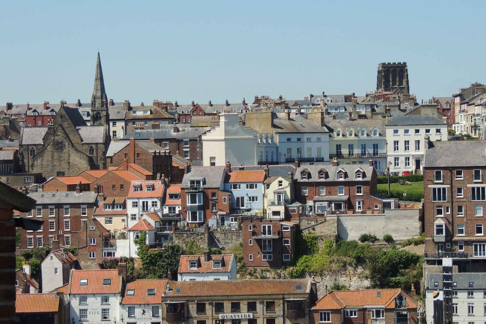 A densely packed coastal town with houses built on a steep hillside, with a church spire and tower visible